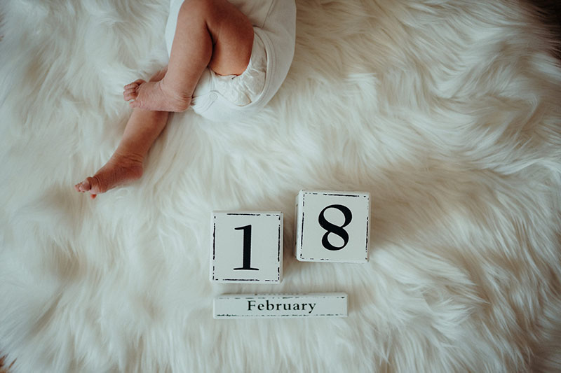 Neugeborenenes Baby mit Kalender auf weißem Fell fotografiert von Marc Feix Photography