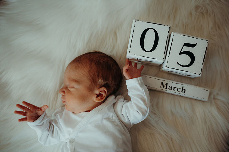 Neugeborenenes Baby mit Kalender auf weißem Fell fotografiert von Marc Feix Photography